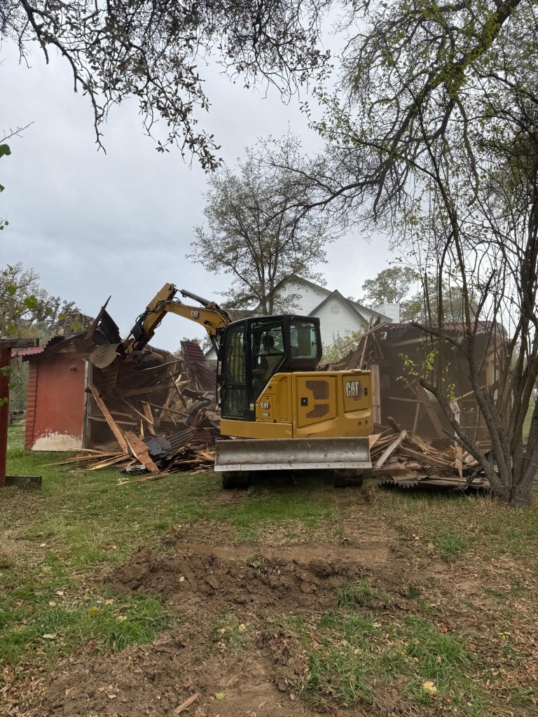Yellow CAT excavator tearing down a red wooden building during a demolition project