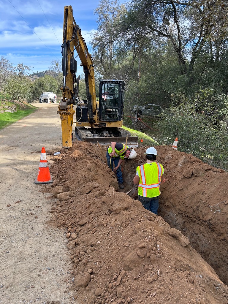 Peak Excavating crew installing underground utilities in a trench next to an excavator